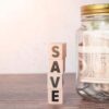 A glass jar labeled for savings sits beside a wooden "Save" sign, emphasizing how breathalysers save you money.