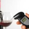 A woman holds a modern breathalyser near a glass of wine, highlighting breathalyser calibration techniques.