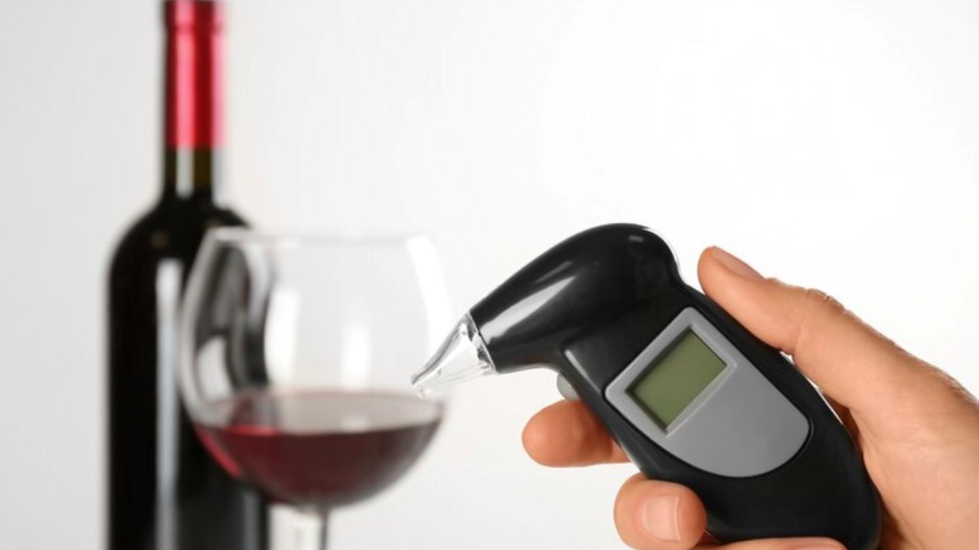 A woman holds a modern breathalyser near a glass of wine, highlighting breathalyser calibration techniques.